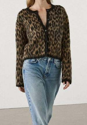 Donna che indossa un cardigan peloso marrone e nero con stampa leopardata, bottoni neri e jeans a vita alta azzurri.