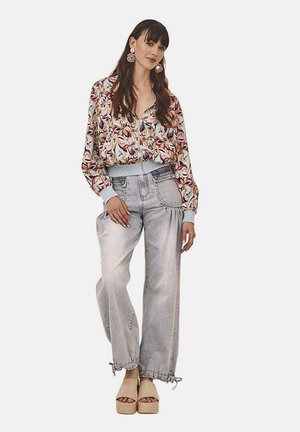 Chaqueta bomber impresa con patrones florales y puños acanalados, combinada con pantalones de mezclilla holgados de lavado claro con dobladillos ajustables y sandalias de plataforma.