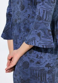 Abito blu con motivo e illustrazioni nere, dotato di maniche a campana e vita arricciata. Il tessuto sembra morbido con una consistenza leggera.