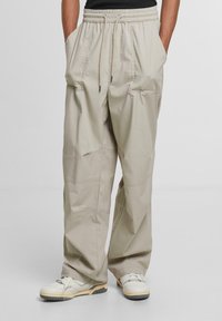 Light beige cargo pants with an elastic waistband, drawstring, two front pockets, and utility seaming detail. Smooth fabric texture.
