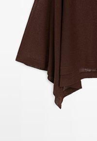 Tessuto marrone scuro con orlo stratificato e fluente, caratterizzato da un taglio asimmetrico e una texture morbida su sfondo bianco.