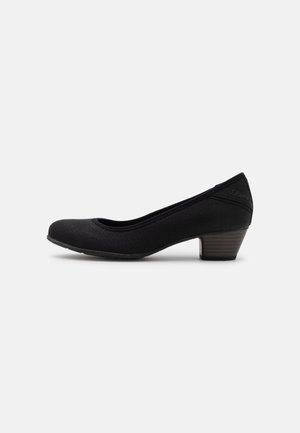 Zapato de mujer negro de tacón bajo con parte superior de tela texturizada y tacón de bloque apilado sobre un fondo claro y liso.