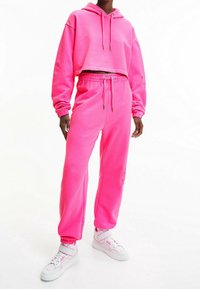 Rosa kortärmad hoodie och matchande joggers i mjukt material, med elastiska muddar och midja, parat med vita sneakers för kontrast.