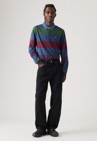 Polo a maniche lunghe a righe blu, verde e bordeaux, con colletto in denim e pantaloni neri larghi. Indossati con sneaker nere.