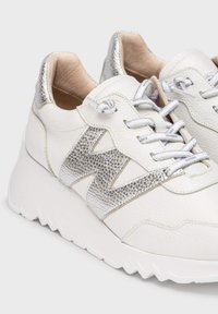 Zapatillas blancas de cuero con un acento plateado texturizado. Presentan una suela gruesa, cordones plateados y un diseño contorneado distintivo.