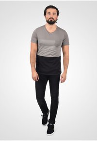 Camiseta color bloqueada en gris y negro con un bolsillo en el lado izquierdo del pecho, combinada con jeans negros y zapatillas negras. Tejido texturizado.