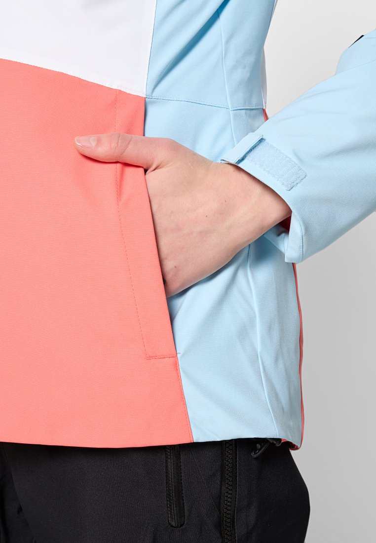 Bunte Sportjacke mit einem Design in Weiß, Hellblau und Koralle. Enthält eine Vordertasche und strukturierte Stoff. Nahaufnahme einer Hand in der Tasche.