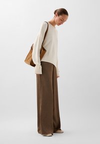 Cremefarvet sweater med lange ærmer og ribbede manchetter, parret med brune vidde bukser og en brun tote bag med en glat tekstur.