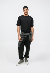 T-shirt preta de manga curta, sweatshirt cinza com fita à cintura, calças pretas largas e ténis cinzentos de cano alto. Design e ajuste simples.