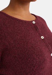 Cardigan bordeaux in tessuto a maglia testurizzata con scollatura arrotondata e due bottoni bianchi frontali per la chiusura.