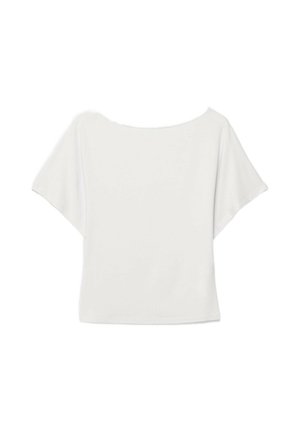 Giovane donna con un vestito bianco a spalle scoperte che cammina, tenendo una borsa argento, in uno spazio interno poco illuminato con dettagli di sfondo minimi.