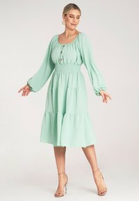 Miętowo-zielona sukienka z długimi bufkowymi rękawami, kwadratowym dekoltem, z guzikami oraz warstwową spódnicą. Wykonana z lekkiego materiału o teksturowanym wykończeniu.
