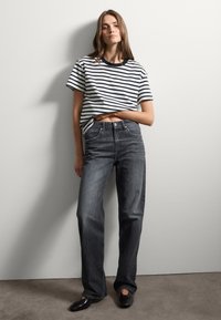Camiseta a rayas con rayas azul marino y blancas, combinada con jeans de mezclilla gris oscuro. Zapatos negros planos completan el atuendo. Diseño simple y casual.