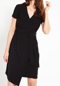 Mustavilla kietaisumekko, jossa on lyhyet hihat, V-mallinen pääntie ja vyötärösidonta. Mekossa on hieman epäsymmetrinen helma ja sileää, kevyttä kangasta.