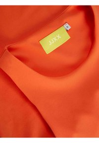 Oranžový textilní top s kulatým výstřihem a hladkým povrchem. Štítek zobrazuje "JJXX" v bílém na jasně žlutém pozadí. Součástí je také velikostní štítek.