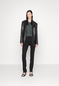 Black leather blazer over a green top, paired with black jeans and black open-toe heels. Smooth texture, tailored fit, and minimalistic design.