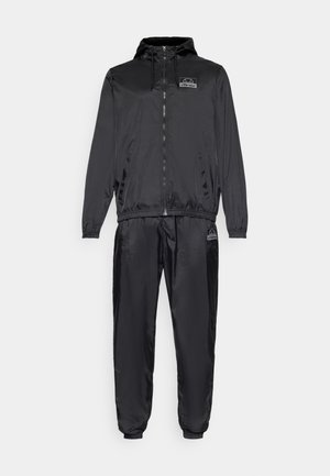 Tuta leggera nera con giacca con zip e cintura elasticizzata. Texture liscia con dettagli in logo sulla giacca e sui pantaloni.