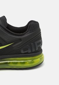 Talons de chaussure de sport noire avec semelle extérieure à coussin d'air vert vif et col en tissu texturé, avec un logo partiel et des trous d'aération.
