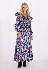 Květinové maxi šaty s námořnickým podkladem, zdobené živými květy v růžové, modré a bílé barvě, s volánovými rukávy, staženým pasem a patrovou sukní. Černé kotníkové boty.