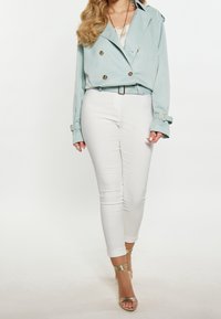 Veste bleu clair croisée à double boutonnage avec des boutons argentés, associée à un pantalon blanc ajusté et des sandales dorées à lanières. Texture de tissu lisse.