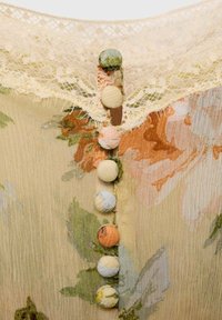 Floral-patterned fabric in soft pastel colors with a delicate lace trim and round fabric-covered buttons along the back.