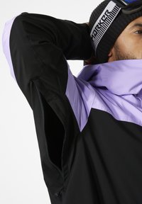 Zwarte en lavendel jas met een hoge kraag, een ritssluiting aan de zijzak en een gladde textuur; heeft een contrasterend kleurblokontwerp.