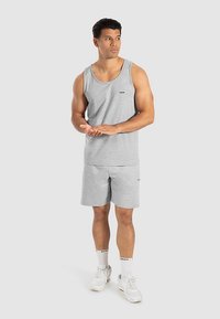 Grijze tanktop en korte broek van een katoenmix. Soepele textuur met een klein logodetail. Witte sneakers en sokken maken de outfit compleet.