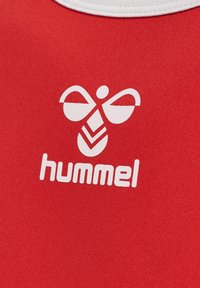 Rød stofsportstrøje med et hvidt "hummel" logo og et karakteristisk grafisk design, der minder om vinger og blade.