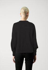Zwarte, oversized sweatshirt met doorgezakte schouders, geribde manchetten en zoom. Gladde textuur met een minimalistisch ontwerp, zonder zichtbare logo's.