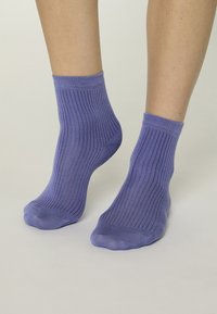 Calcetines tobilleros morados de algodón con una textura acanalada y un ajuste ceñido, que muestran un acabado liso y sin patrones ni detalles visibles.