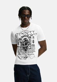 T-shirt bianco in cotone con testo e immagini grafiche nere, girocollo e maniche corte. Il testo include "Nell'ombra dell'Eternità."