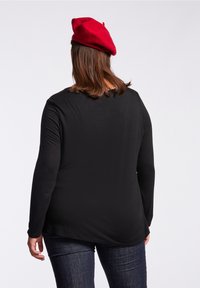 Black long-sleeve shirt with a round neckline, featuring a smooth texture. Paired with denim jeans and a red beret.