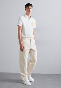 White polo shirt with embroidered logo, paired with light beige cargo pants featuring front pockets and loose fit, complemented by white sneakers.