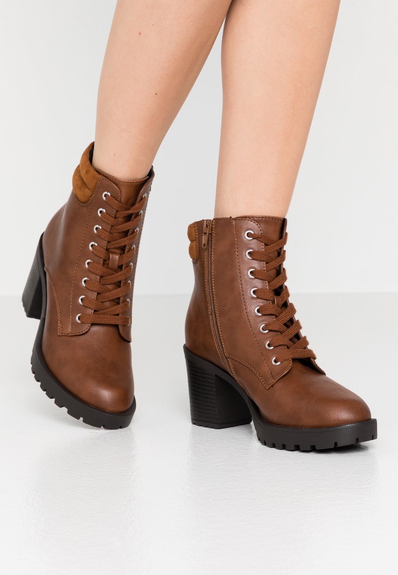Bottines à lacets marron avec une finition en cuir texturé, un talon épais surélevé et une fermeture éclair sur le côté pour plus de praticité. Dispose d'un col de cheville rembourré.