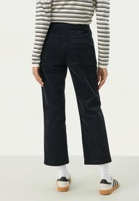 Navyblauwe corduroy wijde broek met achterzakken, gecombineerd met een gestreept shirt met lange mouwen en witte crew-sokken. Casual schoeisel zichtbaar.