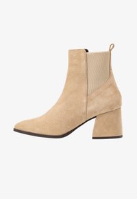 Bottines en suède beige avec un bout pointu, des panneaux latéraux élastiques et un talon carré épais. Avec une languette à l'arrière.