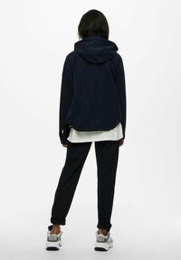 Felpa con cappuccio in fleece blu navy e vestibilità rilassata, dotata di cappuccio e cinturino in vita, abbinata a pantaloni tapered coordinati e una camicia bianca sovrapposta.