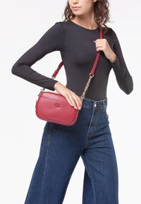 Borsa a tracolla rossa in pelle con catena metallica, forma rettangolare, texture liscia e discreto dettaglio del logo in rilievo.