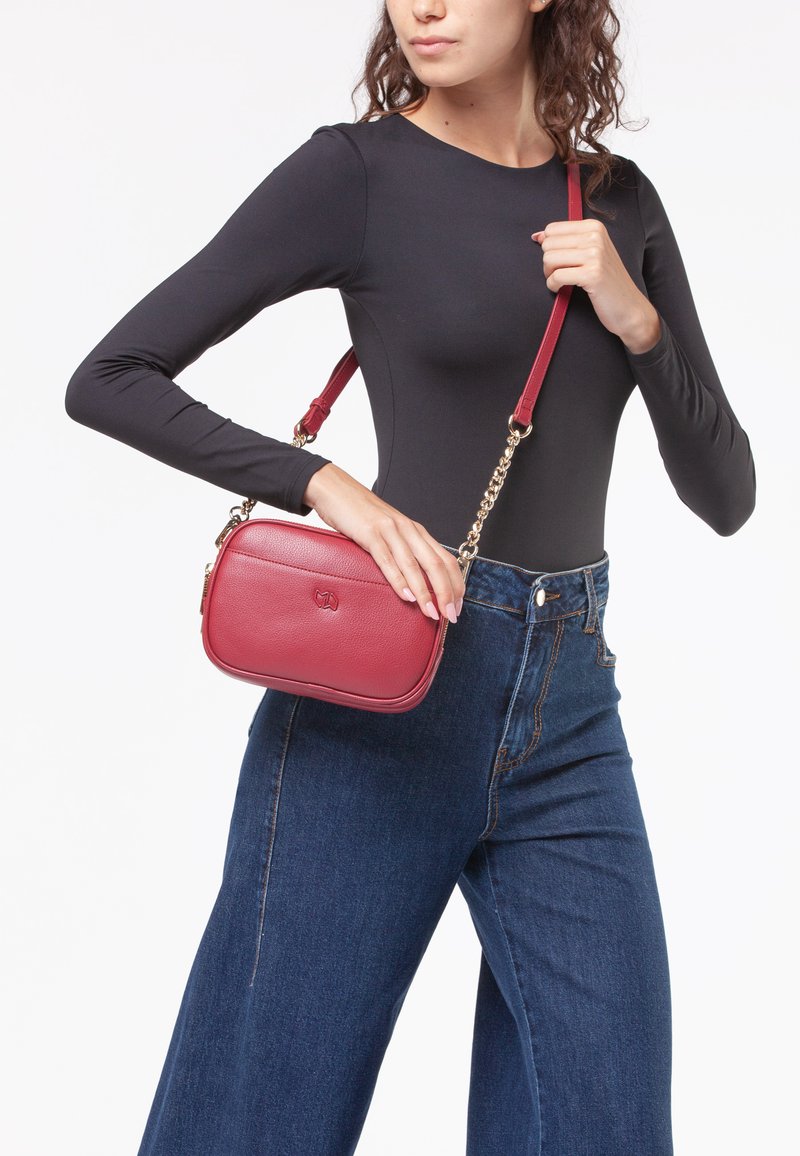 Borsa a tracolla rossa in pelle con catena metallica, forma rettangolare, texture liscia e discreto dettaglio del logo in rilievo.