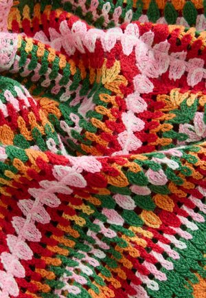 Meerklleurige gebreide deken met rood, groen, oranje, roze en wit garen in een gestructureerd patroon met gekartelde randen en open steken.