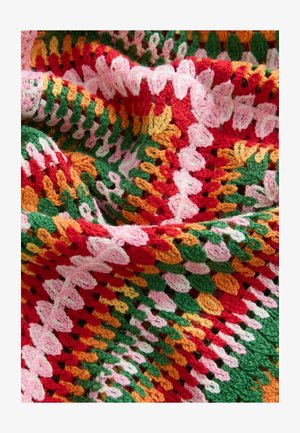 Monivärinen neulottu peitto, jossa on punaista, vihreää, oranssia, vaaleanpunaista ja valkoista lankaa tekstuurillisessa kuviossa, jossa on kaarevat reunat ja avoimia silmukoita.