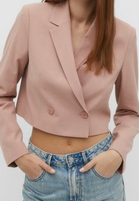 Cropped pink blazer with double buttons, notched lapels, and long sleeves, paired with light blue distressed denim jeans.