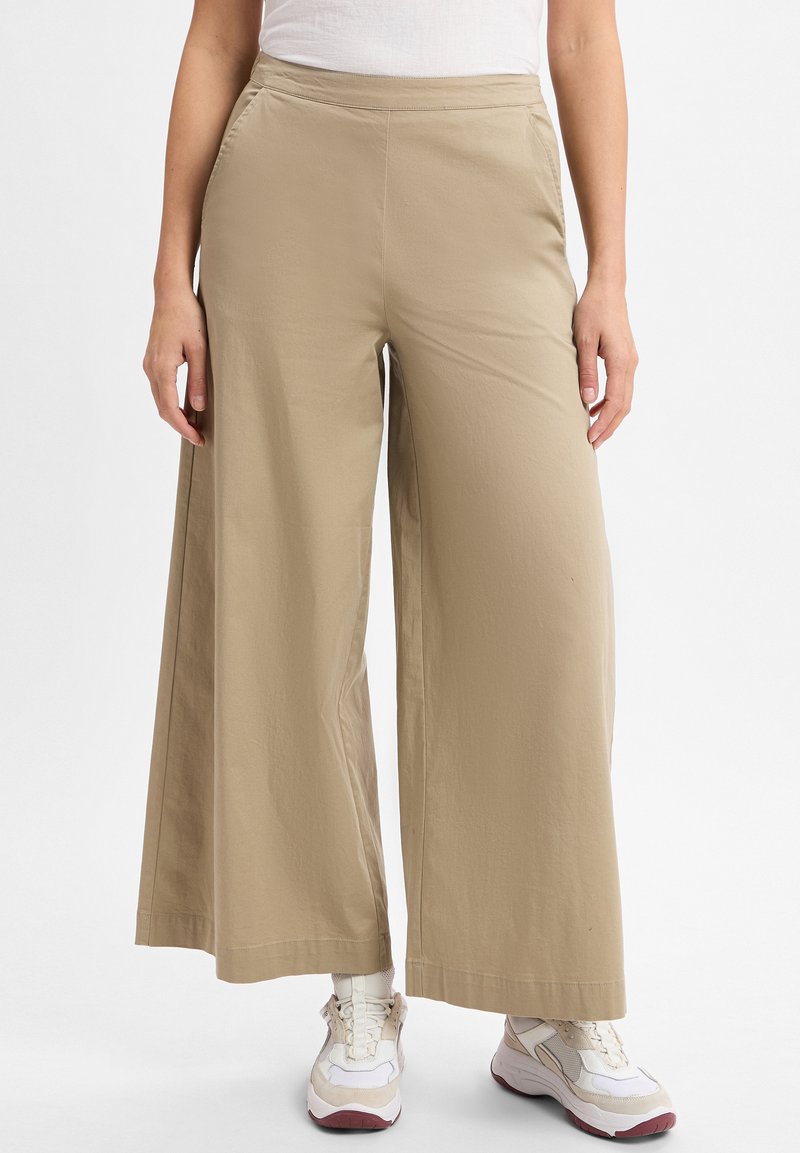 Beige wijde broek gemaakt van lichtgewicht materiaal, met zijzakken en een zachte textuur, gecombineerd met chunky witte sneakers.