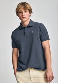 Polo de manga corta en algodón gris oscuro, con un cuello clásico, tapeta de tres botones y un pequeño logotipo bordado en el pecho.