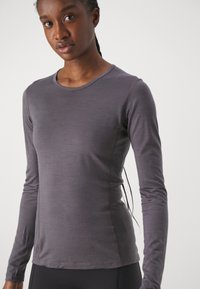 Long-sleeve top in dark gray fabric, smooth texture, fitted design, with a round neckline and contrasting stitching along the sides.
