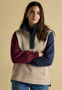 Pulóver v béžovej farbe s farebným prešívaním, s rukávmi v námorníckej modrej, zelenej a burgundskej farbe. Obsahuje štvrtinový zips, stojatý golier a voľný strih. Mäkká textúra.