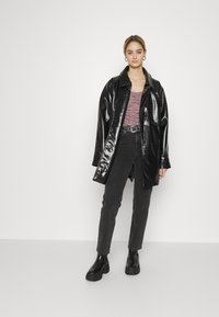 Casaco de imitação de pele preta e brilhante, com um corte descontraído, combinado com uma blusa rosa estampada, jeans cinzentos escuros e botas de tornozelo pretas.