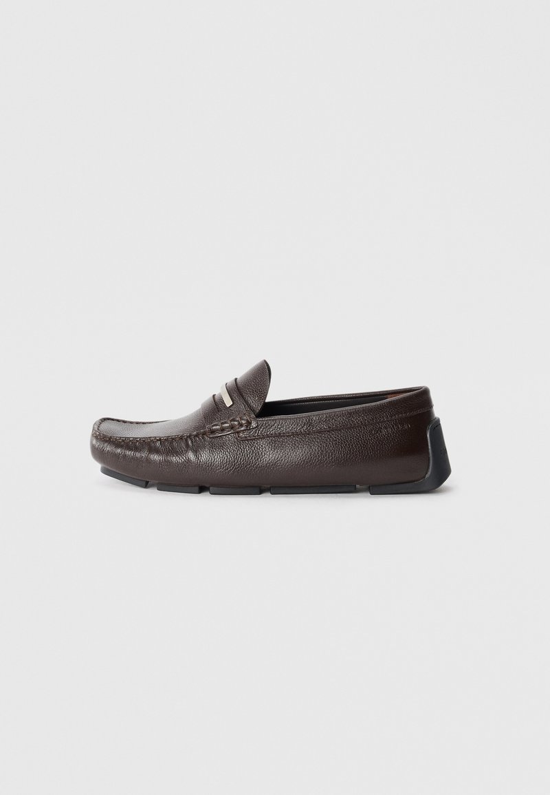 Brown leather loafers with a textured finish, rounded toe, minimal stitching, and a contrast rubber sole. Features a decorative strap accent.
