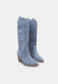 Blå cowboystövlar i mocka med spetsig tå, dekorativa utskärningar och klack i flera lager. Slät textur och mitt på vaden höjd.