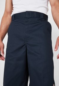Námornícke modré pracovné nohavice vyrobené z odolnej tkaniny s priamym strihom, ktoré majú pás s pútkami na opasok a bočné vrecká. Výrazný detail s logom značky.